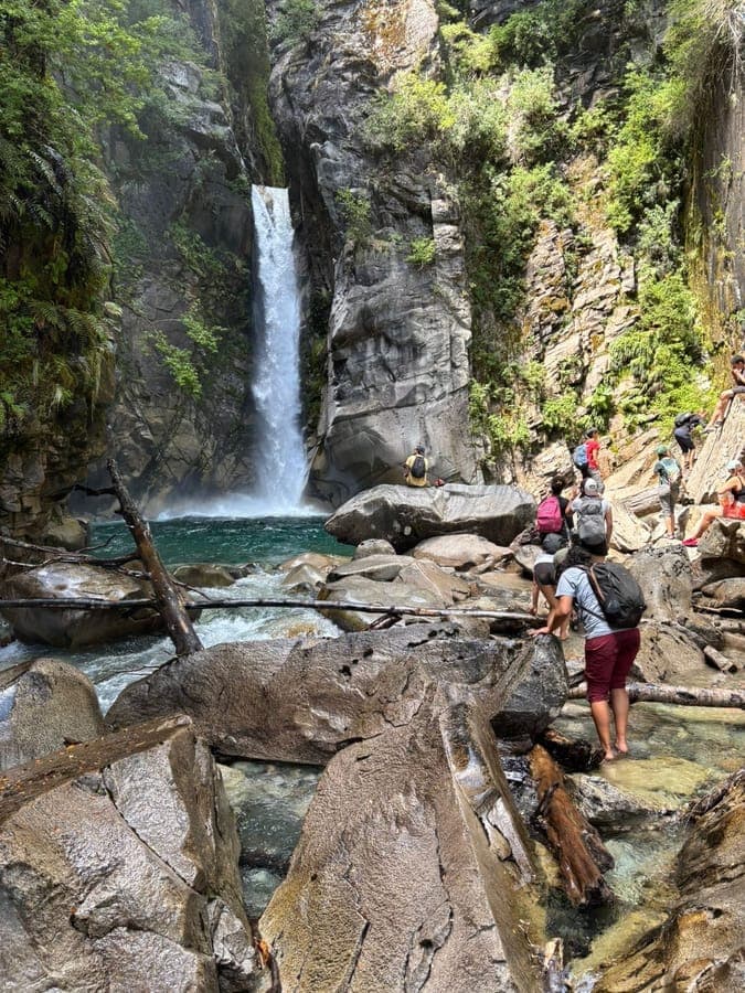Students scrambling over boulders beside a waterfall and turquoise pool in Patagonia.